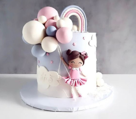  A cake decorated with a girl holding balloons and a rainbow, perfect for a girl's celebration.